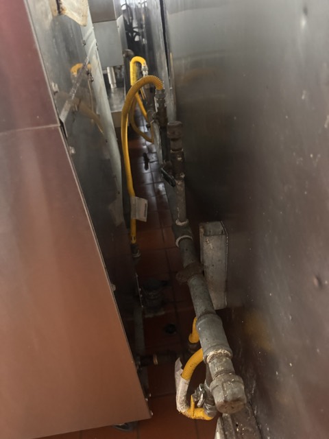 Gas lines behind kitchen equipment exposed for cleaning